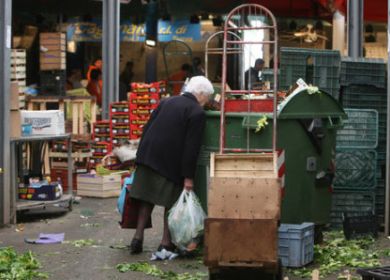 donna anziana che  rovista nei cesti della spazzatura