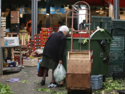 donna anziana che  rovista nei cesti della spazzatura
